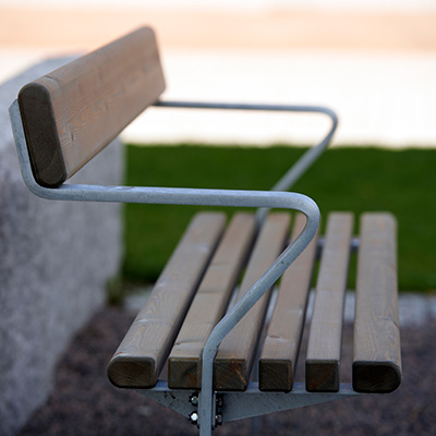 A sideview of a park bench with metal arm rests and frame and a wooden slats for bench and backrest.